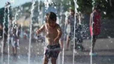 Küçük mutlu bir çocuk yaz tatillerinde açık hava parkında su jetlerine doğru koşuyor.