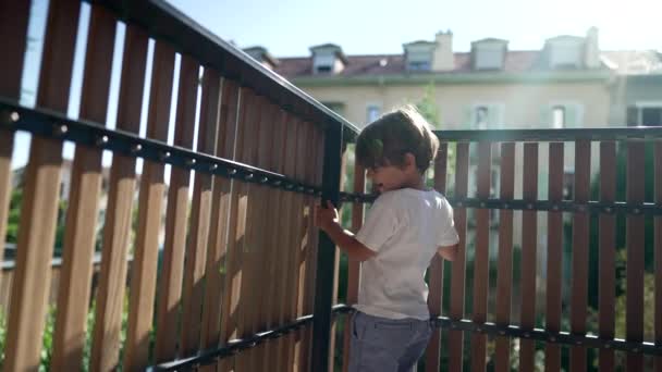 Ένα Μικρό Αγόρι Στέκεται Δίπλα Στο Φράχτη Του Μπαλκονιού Κοιτάζοντας — Αρχείο Βίντεο