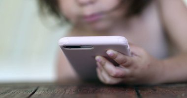 Küçük kız akıllı telefon cihazına bakıyor. Elinde cep telefonu olan bebek çocuk.