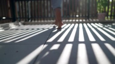 Çocuk ayağı, balkon terasında yürürken, yerde güneş ışığı desenleriyle birbirine yakın.
