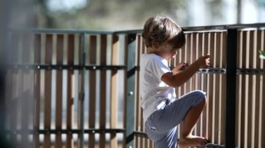 Çocuk apartman binasının balkon ahşap çitlerine tutunuyor. Terasta küçük bir çocuğun güvenliği ve korunması.