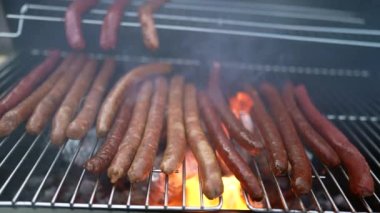 Sosisler ızgarada, alevler yavaş çekimde. BBQ yemeği hazırlanıyor