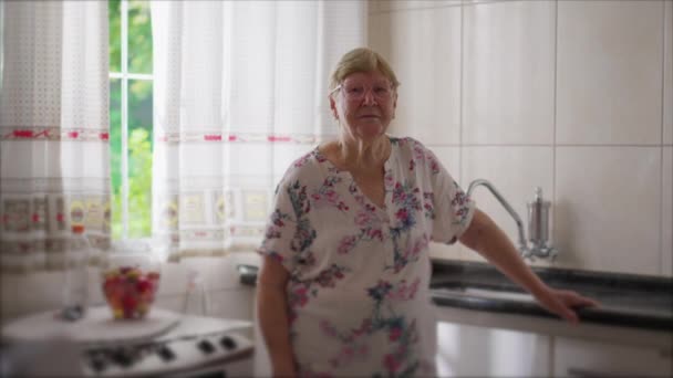老太太站在窗边的厨房里 一位80多岁的老年人凝视着摄像机 真实的家庭生活场景 — 图库视频影像