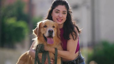 Güneşli bir günde parkta Golden Retriever köpeğiyle poz veren genç bir kadın.