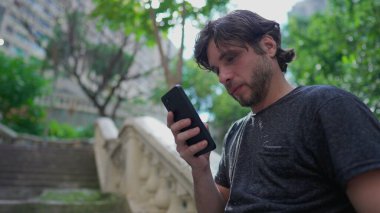 Bir genç, şehir parkının dışında beklerken akıllı telefon cihazından mesaj bildirimi okuyor.