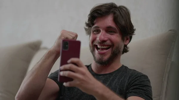Щасливий Чоловік Позитивно Реагує Сповіщення Новин Мобільний Телефон Сидячи Домашньому — стокове фото