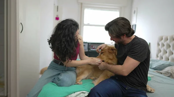 夫妻在家里和狗狗一起玩 坐在床上 年轻男女和他们的金毛猎犬互动 — 图库照片