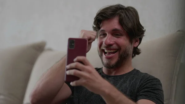 Щасливий Чоловік Позитивно Реагує Сповіщення Новин Мобільний Телефон Сидячи Домашньому — стокове фото