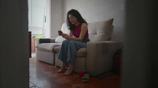 幸せな女性は自宅のアパートでソファに座って電話をチェックします 携帯電話の画面を見ている30代の女性は — ストック写真
