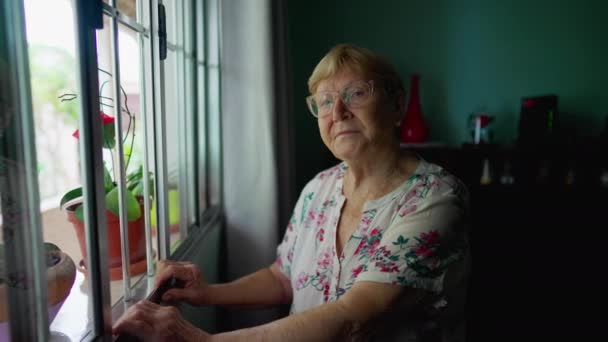 Evde Pencerenin Önünde Duran Kameraya Bakan Yaşlı Bir Kadının Portresi — Stok video