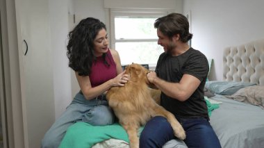 Mutlu çift, Golden Retriever evcil hayvanlarıyla içeride etkileşime giriyor. Bir adam ve bir kadın evlerinde yatarken köpeğini okşuyor.