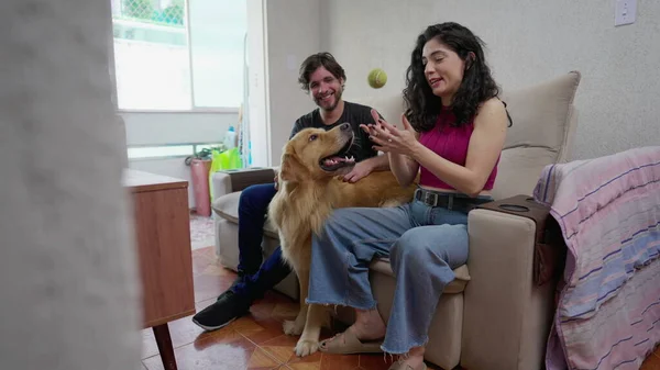 夫妻二人坐在沙发上和他们的狗玩耍 雌性宠物主人和金毛猎犬一起在家里的公寓沙发上玩耍 真实的家庭生活 — 图库照片