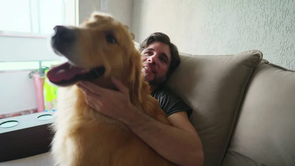 自宅でソファに座っている彼のゴールデンレトリバーと男性犬の所有者 男はペットを愛撫 — ストック写真