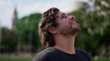 Umutla gökyüzüne bakan genç bir adam. 30 'lu yaşlarda beyaz bir erkek güneşli bir günde başını yukarı çeviriyor.