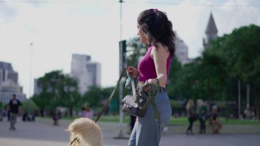 Dişi köpek sahibi Golden Retriever evcil hayvanıyla şehirde yürüyüşe çıkıyor. Günlük yaşam tarzı: Kadın, köpeğini şehir ortamında tasmayla tutuyor.