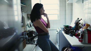 Düşünceli genç bir kadın mutfakta dikilip karar vermeyi düşünüyor. Hayatı düşünen düşünceli bir insanın samimi yaşam tarzı.