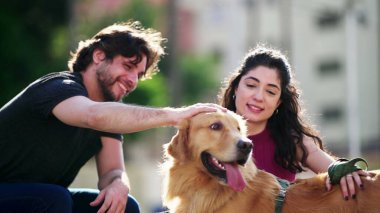 Mutlu çift, Golden Retriever Dog Pet 'leriyle güneşli bir günün tadını çıkarıyor. Erkek ve kadın köpek eşlerini okşuyor.