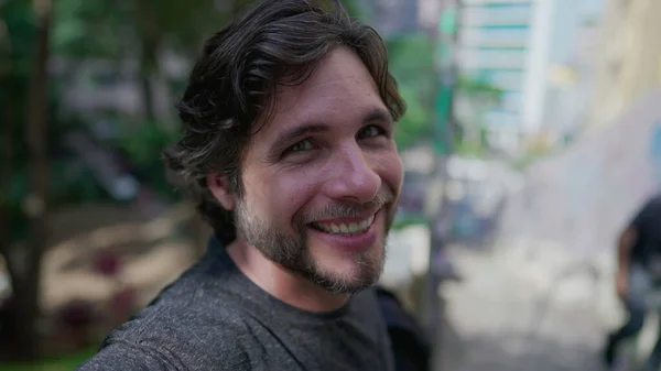 stock image Portrait of a handsome young man standing outside at city park looking at camera smiling. Happy male person in 30s