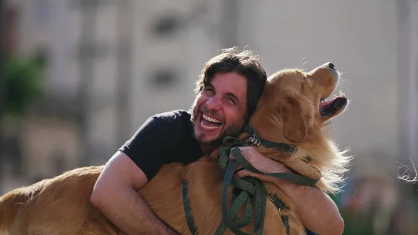 Happy dog owner laughing and smiling while hugging his Golden Retriever dog outside at park