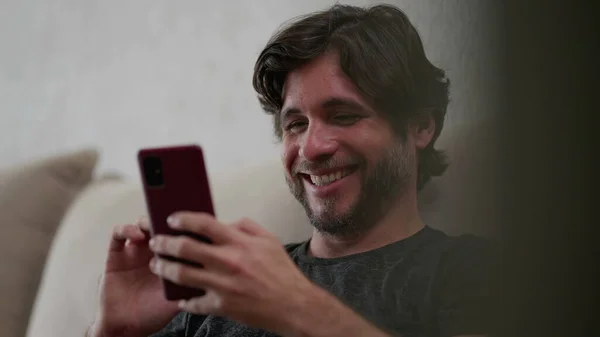 快乐的男人看着家里的智能手机装置 30多岁的男性坐在沙发上 手里拿着手机在社交媒体上打滚 — 图库照片