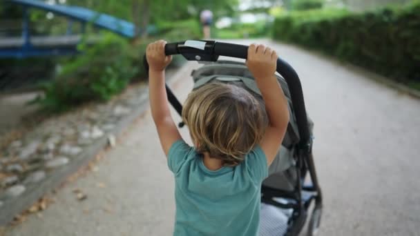 小男孩把婴儿车推到外面的公园 孩子们把婴儿车推到户外 — 图库视频影像