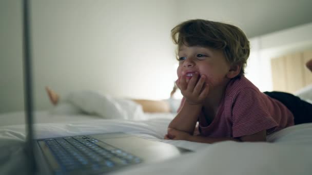 小男孩在晚上躺在床上 在笔记本电脑屏幕上的媒体娱乐节目中扮演主角 晚上被催眠的小孩盯着蓝色发光的屏幕 — 图库视频影像