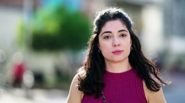 Dışarıda doğal bir ifadeyle duran kameraya doğru sabırlı bir şekilde başını çeviren genç bir kadının portresi.