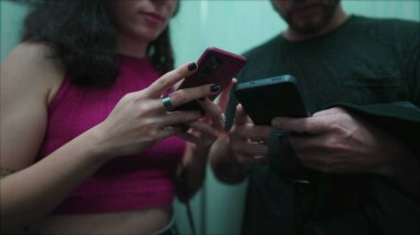 Asansörde cep telefonlarına bakan bir çift. Kadın ve erkek asansörde vakit geçirmek için telefonlarına bağımlı oldular. Yakın çekim elleri modern teknoloji cihazlarını tutuyor.