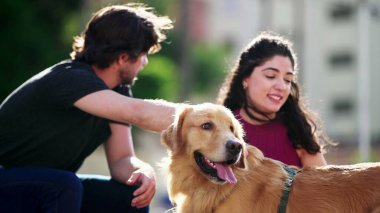 Mutlu çift, Golden Retriever Dog Pet 'leriyle güneşli bir günün tadını çıkarıyor. Erkek ve kadın köpek eşlerini okşuyor.