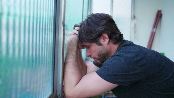 stock image Stressed man struggling with mental illness leaning by window suffering from emotional despair. One worried male person in 30s feeling pressure