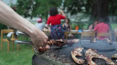 Güneşli bir günde açık hava partisinde barbekü ızgarası hazırlayan klempi yakın çekimde tutuyorum. Pirzola ve yemek BBQ 'da kapanıyor.