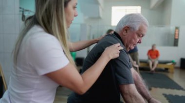 Kadın Pilates eğitmeni yaşlı adama fizik tedavi stüdyosunda egzersiz yaptırıyor.