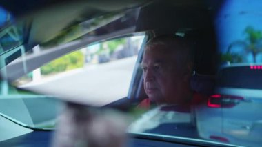 Şehrin sokaklarında trafikte sıkışan son sınıf öğrencilerinden biri dikiz aynasından görülüyor. Yaşlı sürücü araçların arkasında durmuş.