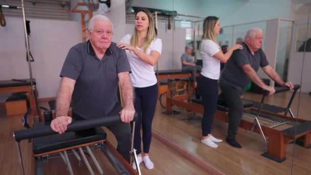 Pilates Instructeur Begeleiden Oudere Man Oefenen Met Machine Fysiotherapie Studio — Stockvideo