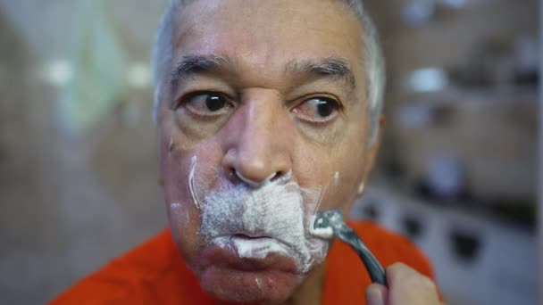 バスルームの鏡の前でひげを剃る老人は 高齢者の家庭生活の朝の儀式 クローズアップ顔 — ストック動画