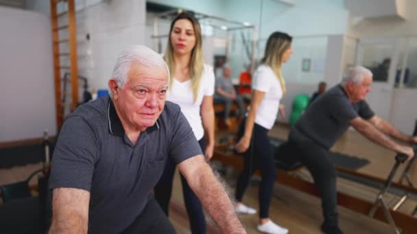 老年男子运动指导健身 普拉多工作室与女教练交谈 老年人使用机器伸展 照顾脊柱健康 — 图库视频影像
