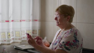 Evde cep telefonu kullanan yaşlı bir kadın. Telefon cihazına mesaj yazan yaşlı kadın, modern teknolojiyi kullanan yaşlı kişi.