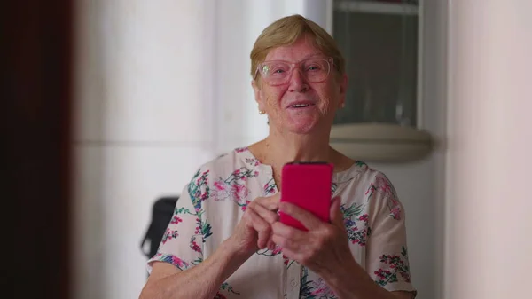 Šťastná Starší Žena Držící Zařízení Smartphonu Dívající Kameru Úsměvem Domácí — Stock fotografie