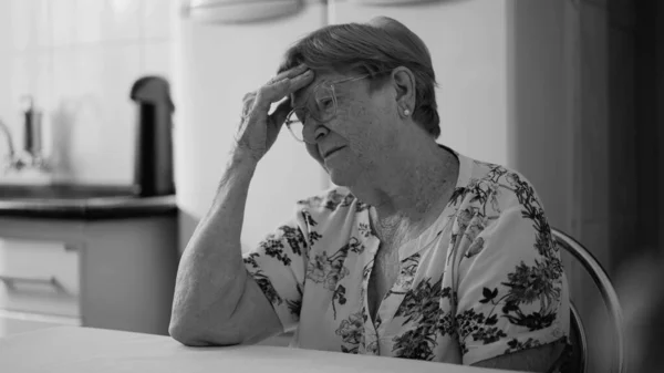 抑圧されたシニア女性で彼女の80表現孤独と孤独 でキッチンに座ってモノクロ黒と白 — ストック写真