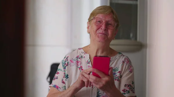 Šťastná Starší Žena Držící Zařízení Smartphonu Dívající Kameru Úsměvem Domácí — Stock fotografie