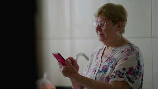 老年妇女在手机上浏览互联网 精通技术的老年人在家从事现代技术工作 — 图库照片
