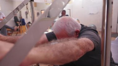 Pilates Stüdyosu Grup Toplantısı 'nda egzersiz yapan yaşlı kişi. Yaşlı bir beyaz adam makineyle vücuduna bakıyor.
