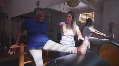 Yaşlı Siyahi Kadın Pilates Oturumunda Esneme Bacağı ve Vücut, Koç Eğitmen 'in rehberliğinde Yaşlılara Omurga Sağlığını Destekleme Programı