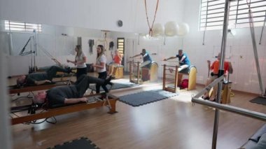 Pilates Stüdyosunda egzersiz yapan bir grup yaşlı insan. Yaşlılık egzersizleri. Yaşlılara vücut geliştirme ve esnetme eğitimi veren kadın antrenör