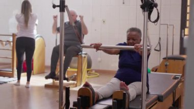 Üst düzey egzersiz Pilates Grubu sınıfında, vücudu güçlendirmek için makine kullanan siyah bir kadın. Yaşlılık egzersizi yaşam tarzı