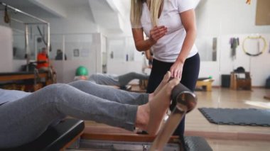 Pilates Stüdyosunda egzersiz yapan son sınıf öğrencisi. Yaşlı kadın, kadın koçun yardımıyla makina esneme egzersizi yaparak uzanıyordu.