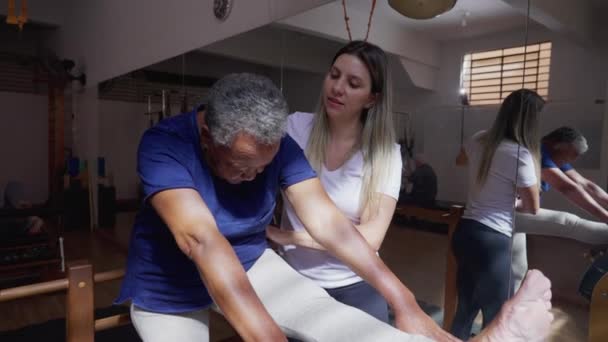 普拉多老师引导一位非裔美国老年黑人妇女伸展身体和腿 老年人在老年锻炼时照顾脊椎健康 — 图库视频影像