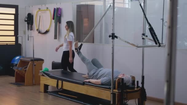 Pilates Instruktor Unterstützt Seniorin Bei Stretching Übungen Während Rehabilitationseinheit — Stockvideo