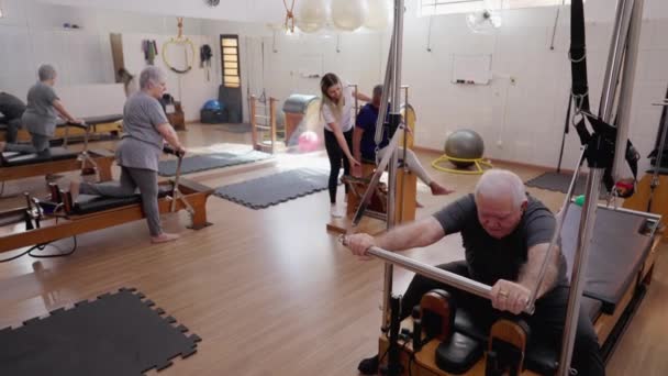 长者使用普拉提机进行小组训练 女教练指导老年人活动和伸展身体 老年人的日常锻炼 — 图库视频影像
