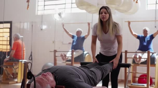 Trener Pilates Pomaga Starszemu Człowiekowi Używać Maszyny Wzmacniania Ciała Nóg — Wideo stockowe